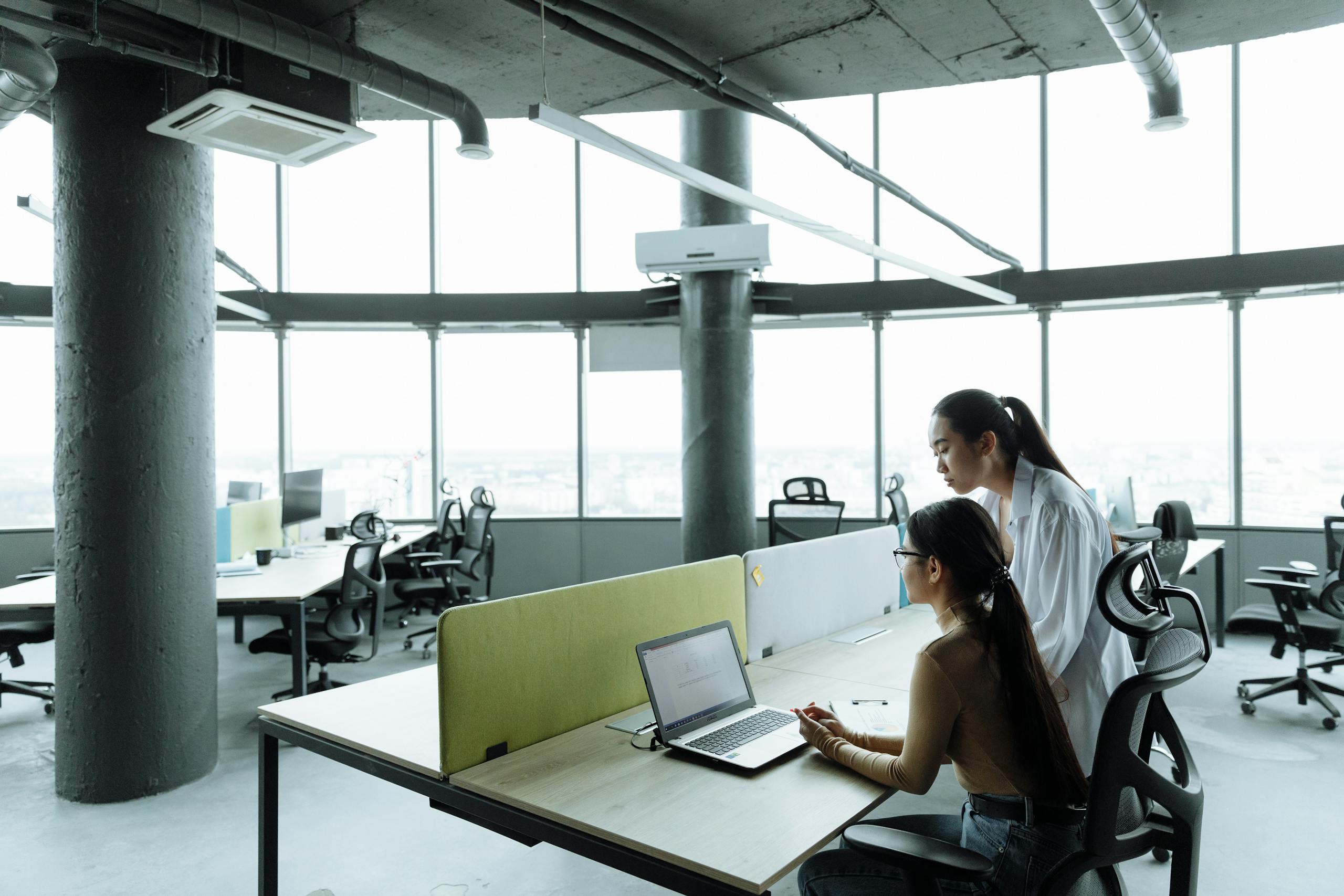 Two Asian women collaborating in a modern office environment focused on teamwork and innovation.